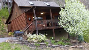 A rustic log cabin with a balcony, surrounded by trees and a small garden. - Cozy & Perfect For A Romantic Getaway For Two! (Pigeon Forge)