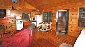 A cozy cabin interior with a wooden interior, a dining area with a table and chairs, a kitchen with a stove and refrigerator, and a red sofa. - Cozy & Perfect For A Romantic Getaway For Two! (Pigeon Forge)