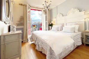 A bedroom with a large bed, a dresser, a nightstand, a chandelier, and a balcony with a view of the city. - One-of-a-Kind 3-bedroom OMG Eiffel Views & Wraparound Terrace (Paris)
