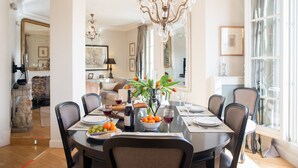 A dining area with a round table set for six, surrounded by chairs. A chandelier hangs above, and the room has a large window with curtains. - One-of-a-Kind 3-bedroom OMG Eiffel Views & Wraparound Terrace (Paris)