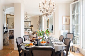 A dining area with a round table set for six, surrounded by chairs. A chandelier hangs above, and the room has a large window with curtains. - One-of-a-Kind 3-bedroom OMG Eiffel Views & Wraparound Terrace (Paris)