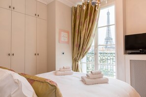 Quarto de hotel com cama, guarda-roupa, janela e vista para a Torre Eiffel, e uma TV Samsung.