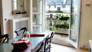 A room with a dining table, chairs, a mirror, and a view of a balcony with plants and a building. - One-of-a-Kind 3-bedroom OMG Eiffel Views & Wraparound Terrace (Paris)