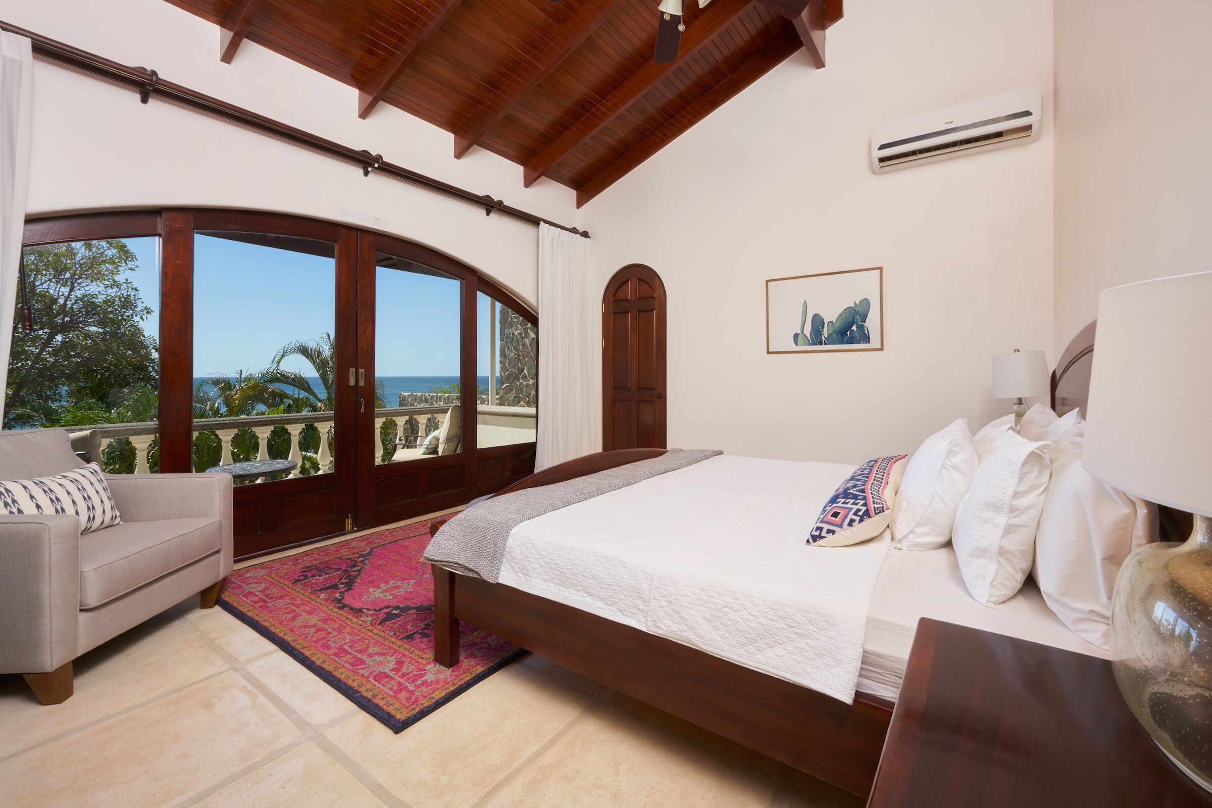 Een slaapkamer met een groot bed, een slaapbank, uitzicht op zee en een balkon.