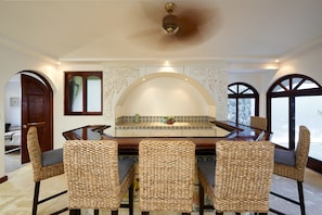 A dining area with a round table, four woven chairs, a ceiling fan, and decorative wall panels.
