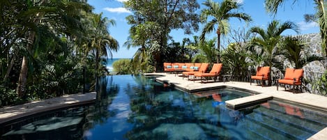 An infinity pool with orange lounge chairs and palm trees.