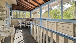 A covered porch with a wooden ceiling, white railings, and a view of trees. There are plastic chairs and a small table with a lamp. - Charming home, perfect for families, Bikers,  Brevard College, College,  camps  (Brevard)