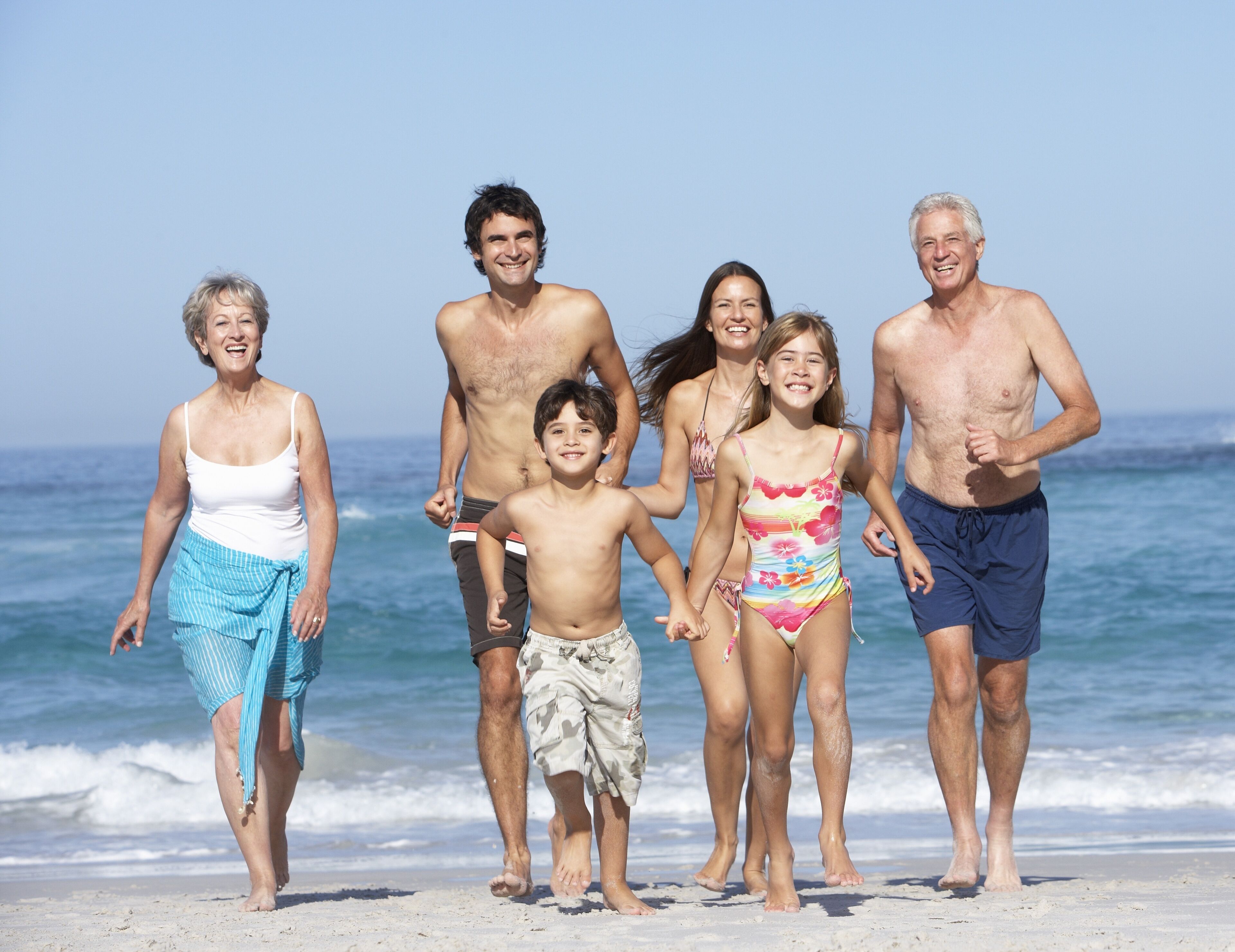 A family of six on a beach with clear skies and ocean in the background.