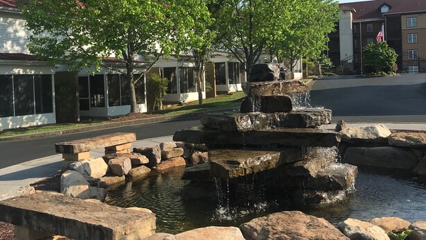Een stenen fontein met water dat over rotsen stroomt, omringd door een verhard gebied met mulch.