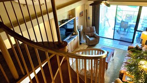 Eine Wendeltreppe führt zu einem Wohnbereich mit einer Couch, einem Sessel und einem Fernseher.