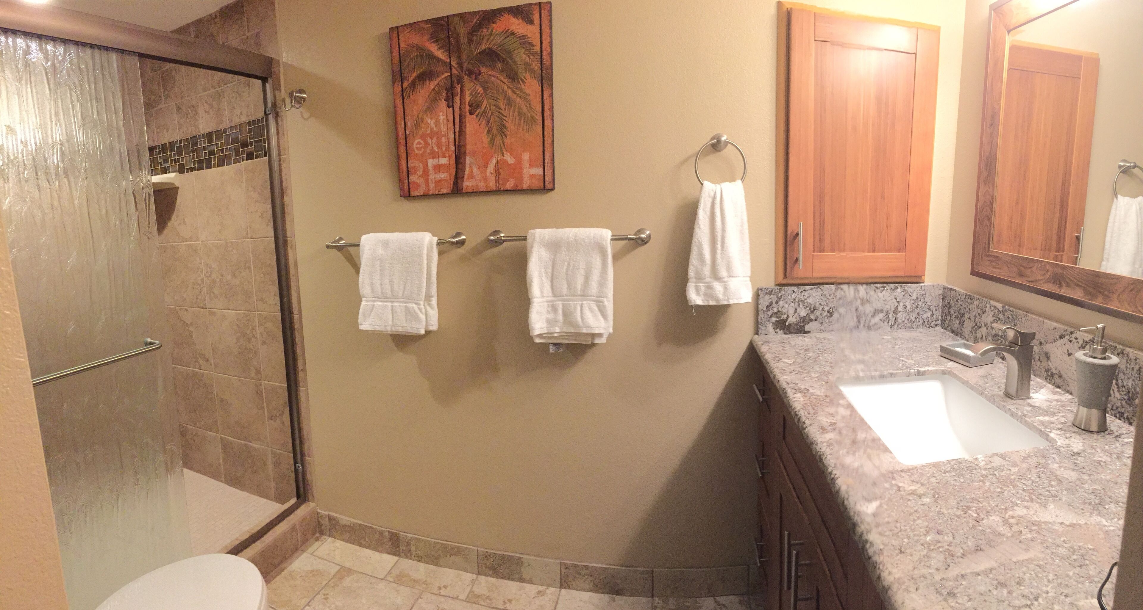 A bathroom with a shower, a sink, and a toilet. There are towels hanging on a rack.