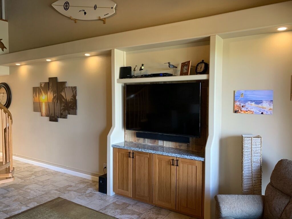A living room with a built-in entertainment center, a large flat-screen TV, wooden cabinets, and a decorative wall piece.