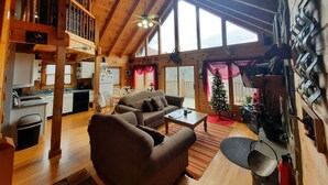 A spacious living area with a high ceiling, wooden beams, a dining area, and a kitchen.
