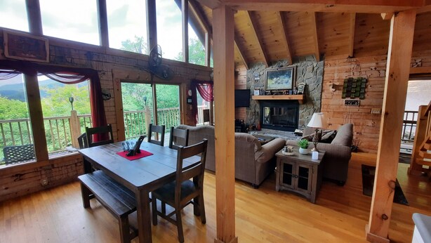 A cozy cabin interior with a wooden dining table, chairs, a sofa, and a fireplace.