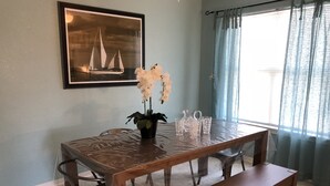 Uma área de refeições com mesa de madeira, cadeiras, um banco, um quadro emoldurado, uma orquídea em vaso e um jarro.