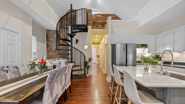 A modern kitchen with a central island, a spiral staircase, and a dining area with patterned chairs.