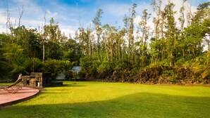A well-maintained grassy area with a stone wall and a small structure. - Affordable Luxury on Kaloli Point.  (Keaau)
