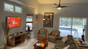 A living room with a television, wicker furniture, a ceiling fan, and a view of the outdoors. - Affordable Luxury on Kaloli Point.  (Keaau)