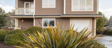 Une maison à deux étages avec un balcon à l’étage supérieur, un garage et un jardin bien entretenu agrémenté d’une grande plante d’agave.
