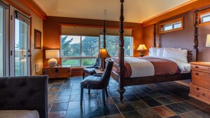 A spacious bedroom with a four-poster bed, a desk with a chair, and a view of the outdoors through large windows. -  Beach House W Ocean Views, 3 Golfer en suites, hot tub, fireplace, Pets OK! (Bandon)