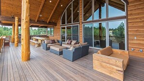 A spacious outdoor deck with wooden furniture, large windows, and a wooden ceiling.