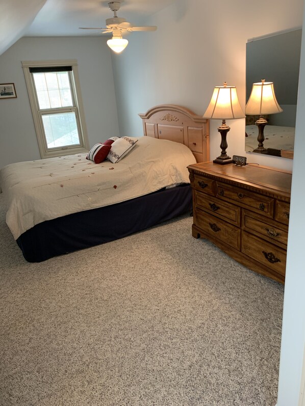 A bedroom with a bed, a dresser, a ceiling fan, a window, and a mirror.
