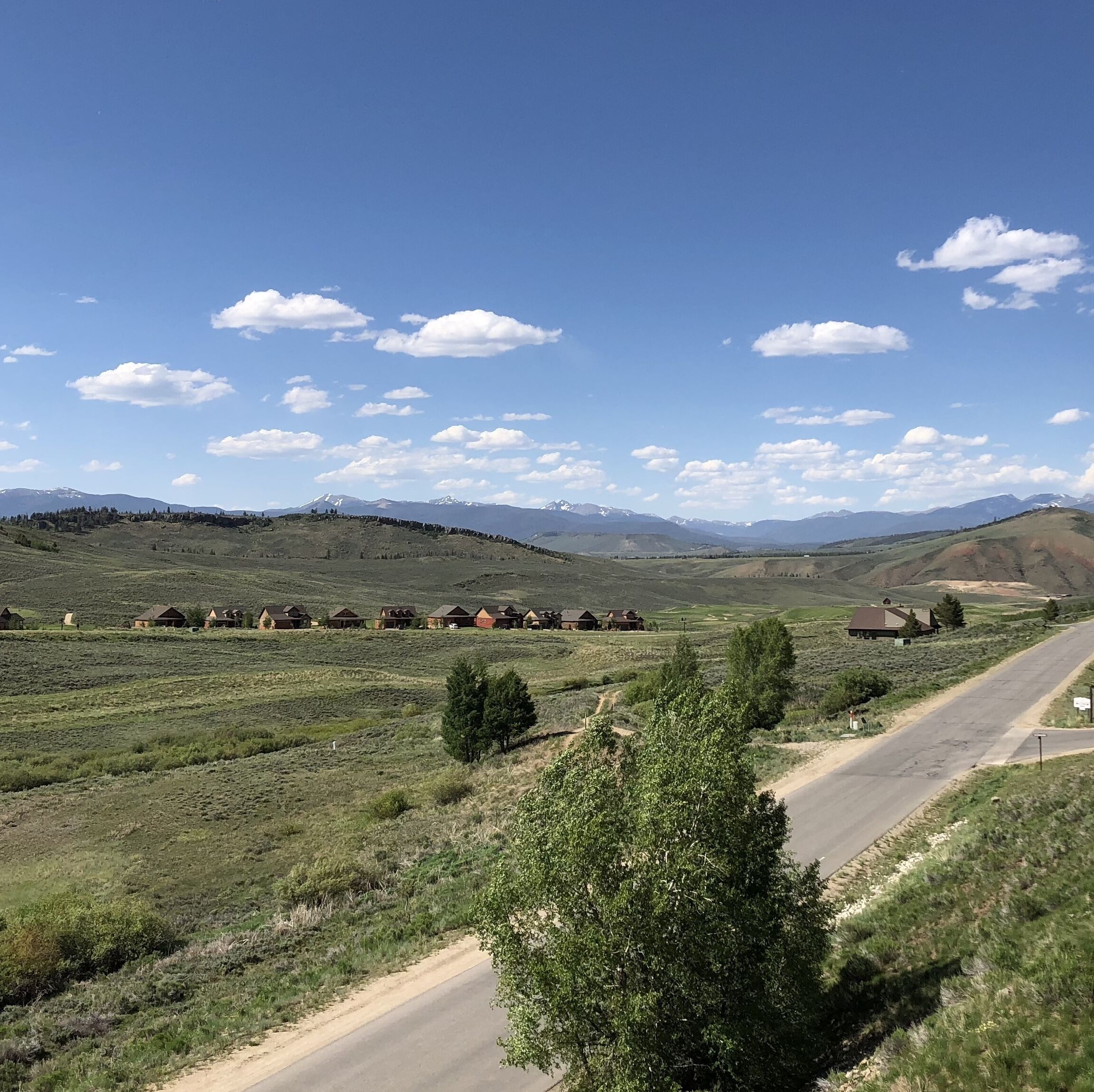 A rural landscape with a road, houses, and mountains in the background.