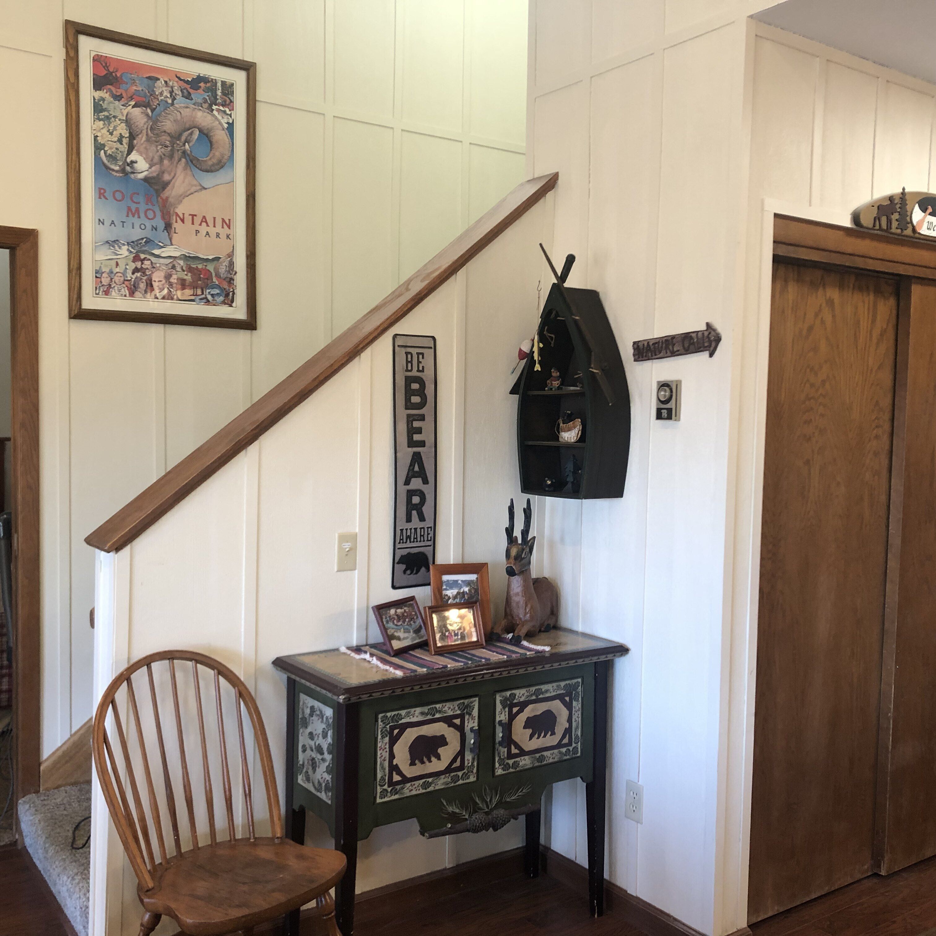 A staircase with a wooden handrail, a small table with a bear-themed design, a chair, and a wall-mounted shelf with decorative items.