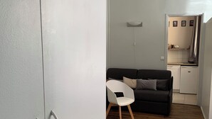 A room with a wardrobe, a sofa, a small table, and a kitchen area.