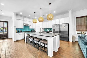 A modern kitchen with white cabinets, a large island with bar stools, a stainless steel refrigerator, and pendant lighting. - Hollywood & Divine | Luxury Frangista Beach Vacation Rental | Huge Private Pool, Game Room, Close to Beach! (Miramar Beach)