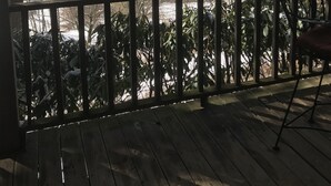 A wooden deck with a metal railing, overlooking a snowy landscape with trees and a mountain in the background.