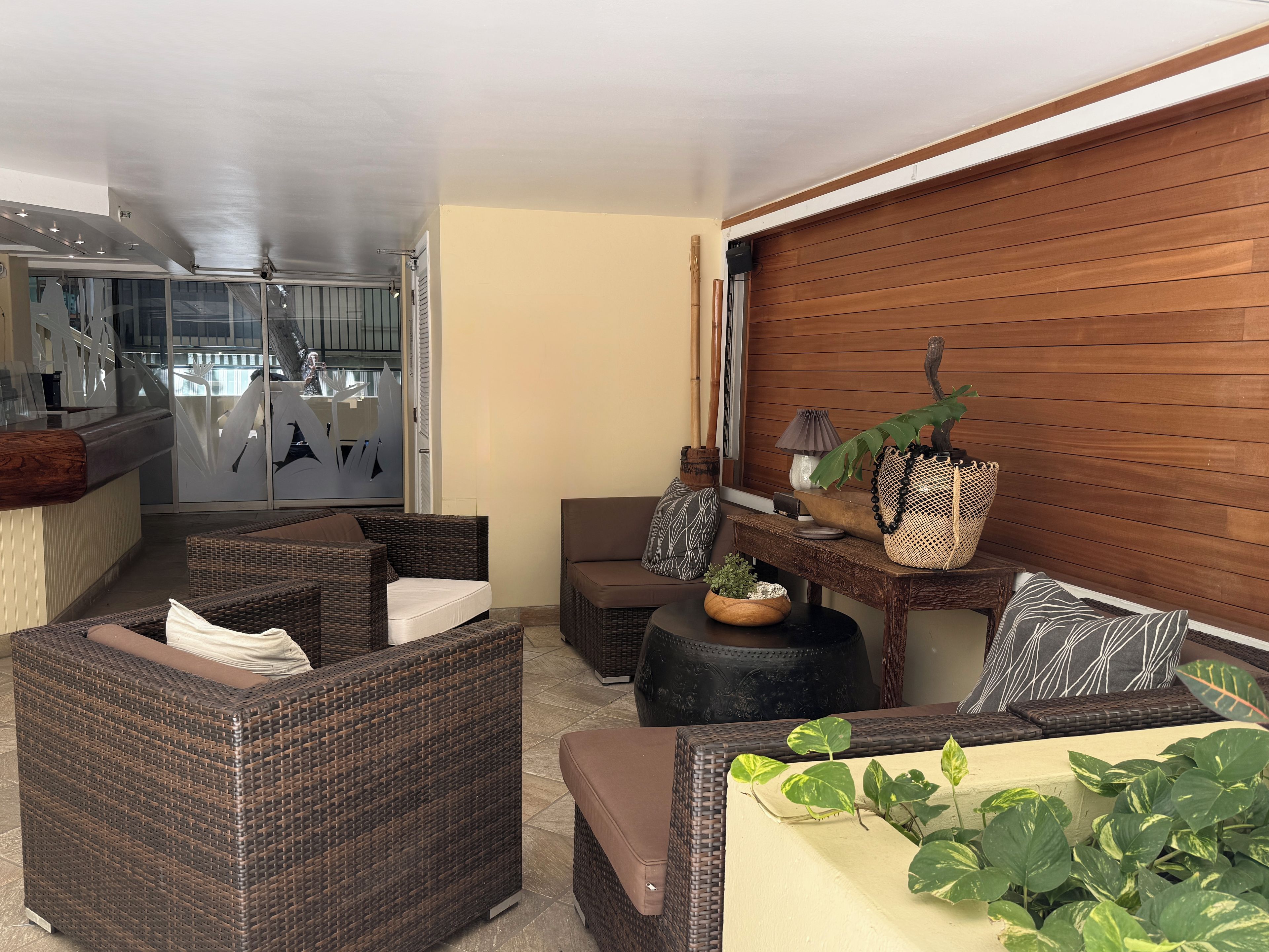 Un espacio moderno con mobiliario de mimbre, una pared de madera y vista a la cocina.