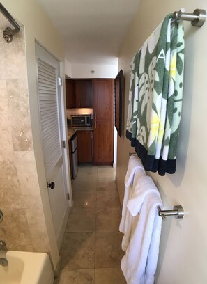 A narrow hallway with a bathroom on the left, a kitchen area in the middle, and a towel rack with a patterned towel on the right.