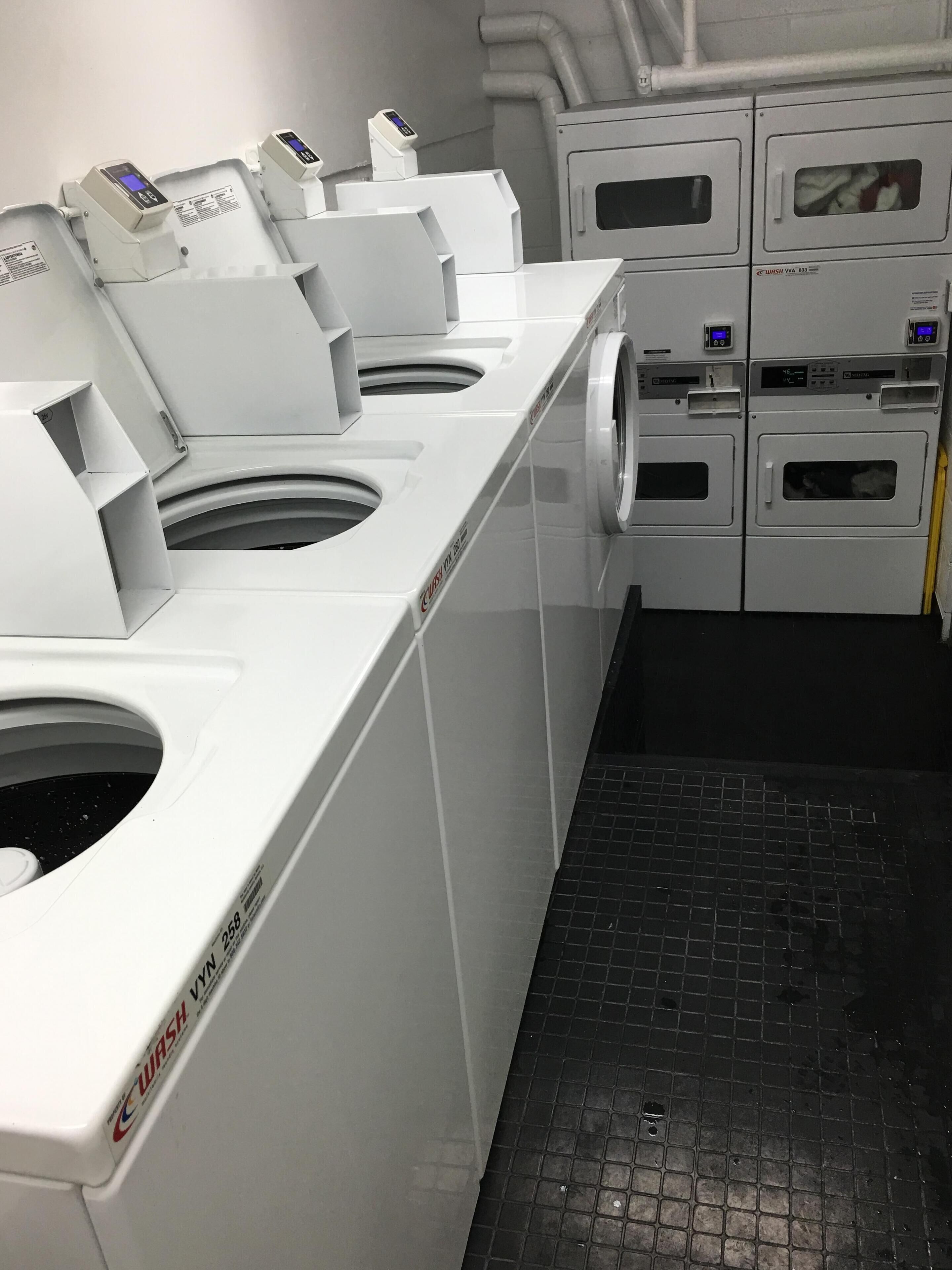 Een rij witte wasmachines en drogers in industriële stijl, met digitale displays, in een compacte, functionele ruimte.