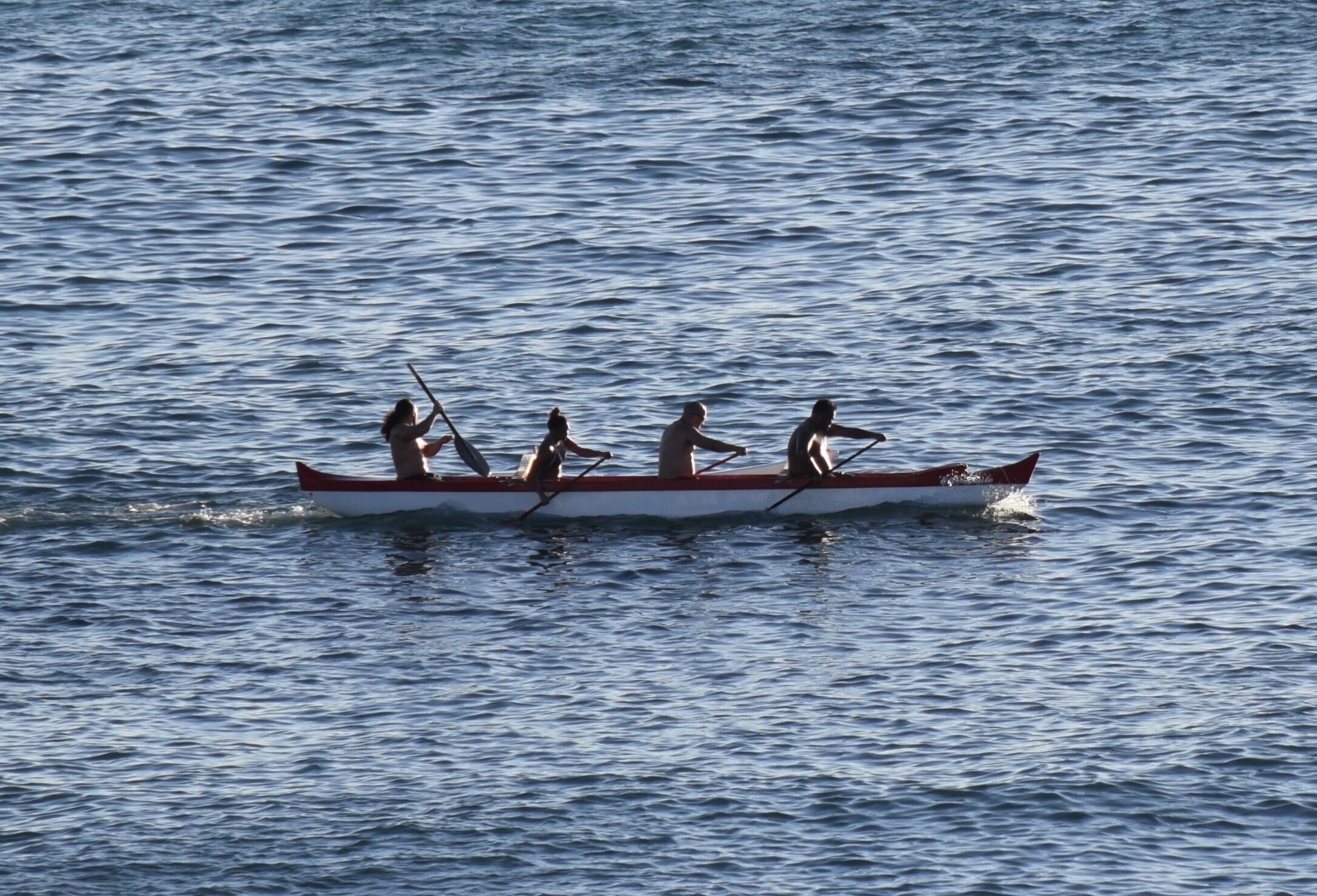 Ein Ruderboot mit vier Ruderern auf ruhigem Gewässer.
