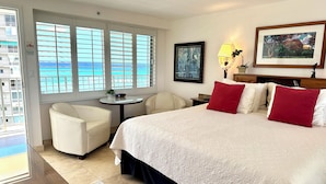 Une chambre d’hôtel avec un lit, deux chaises, une petite table, une lampe et un tableau.
