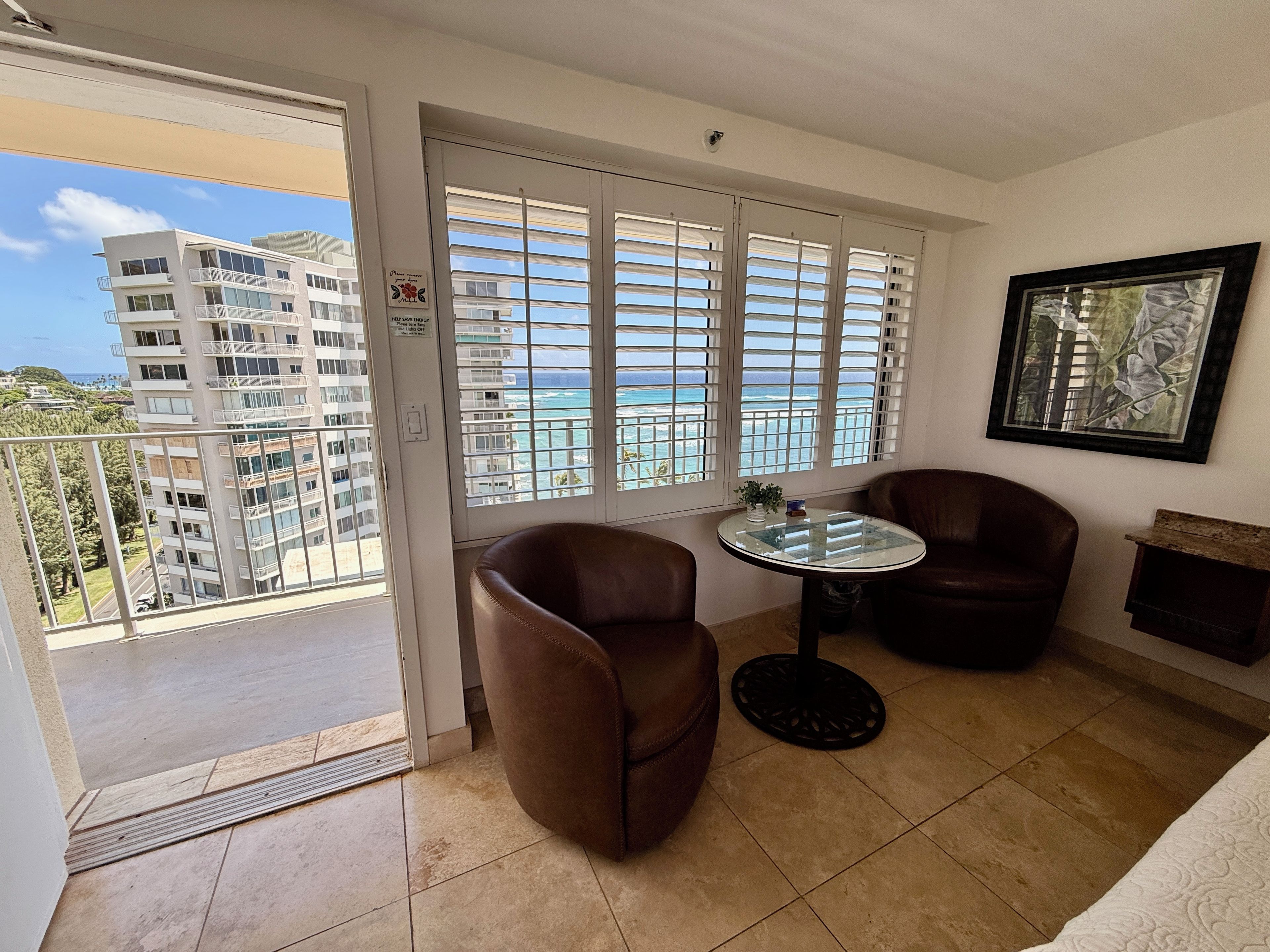 Un balcon donnant sur un immeuble et l’océan, aménagé avec deux chaises et une petite table.
