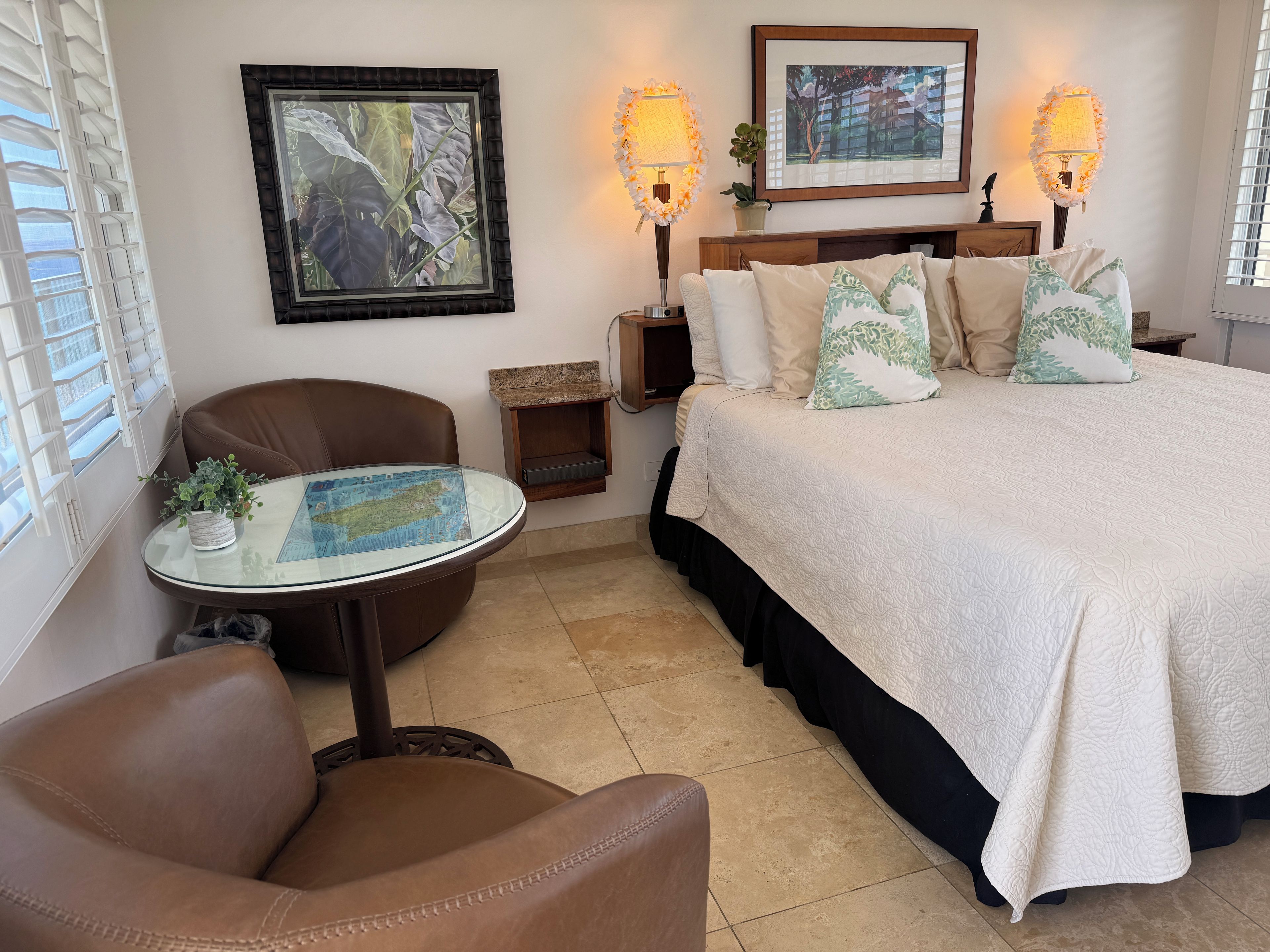 A hotel room with a bed, a chair, a small table with a map, two wall-mounted lamps, and a framed picture.