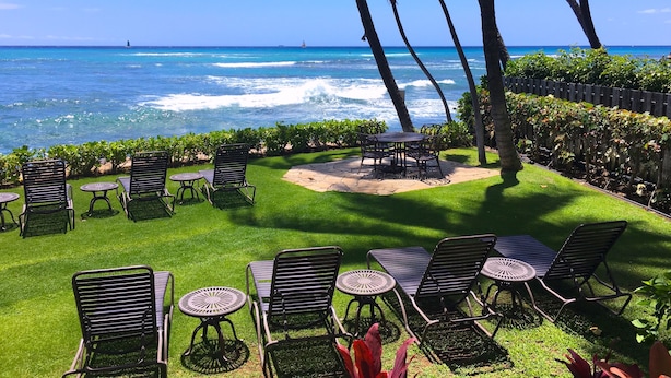 Une terrasse avec des sièges extérieurs, une vue sur l’océan et des palmiers.