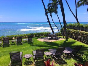 A patio with outdoor seating, a view of the ocean, and palm trees.
