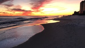 Ein Strand mit Sonnenuntergang, Wellen und einem Gebäude im Hintergrund.