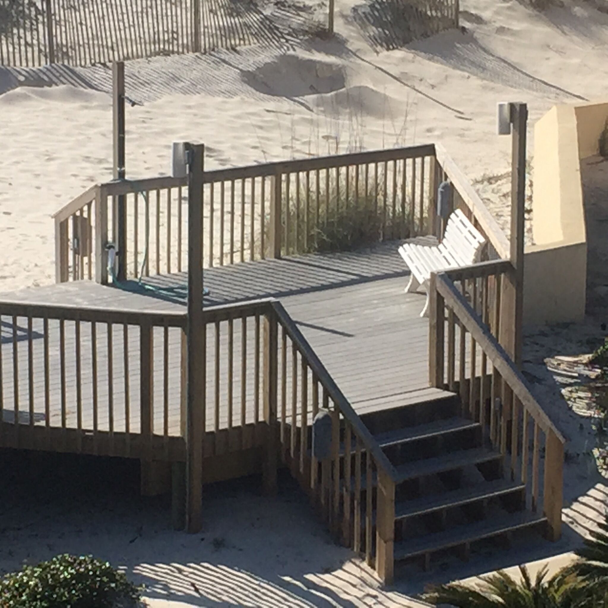 A wooden deck with a bench, surrounded by sand dunes.