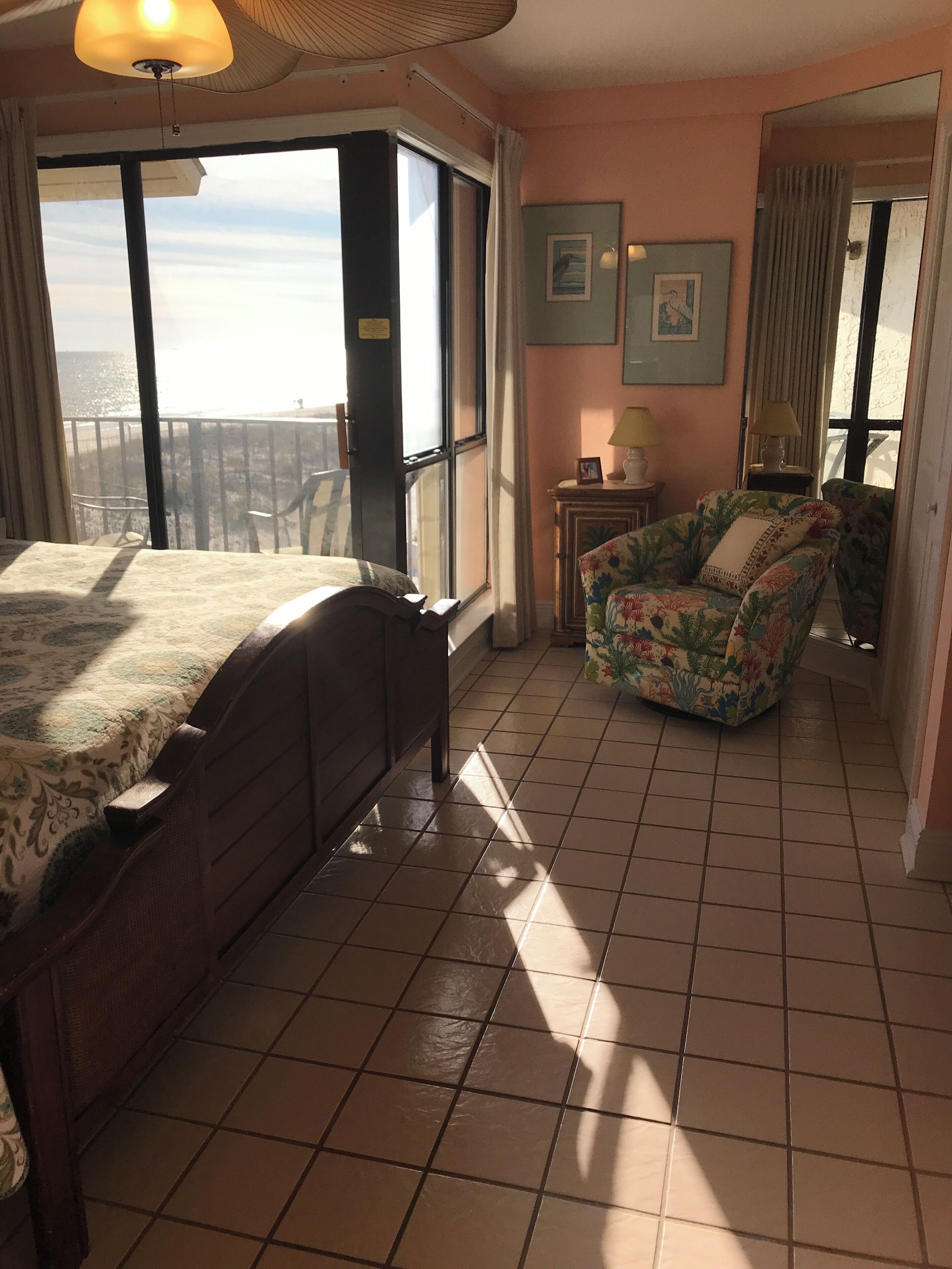 A bedroom with a bed, a chair, a small table, and a view of the sea.