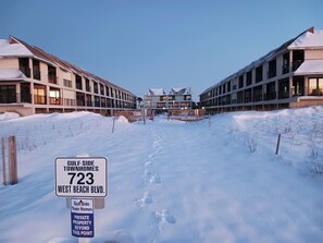 Un camí cobert de neu que condueix a un edifici amb nombroses balconades i un senyal que diu 'Gulf Side Town Homes 723 West Beach Blvd.'