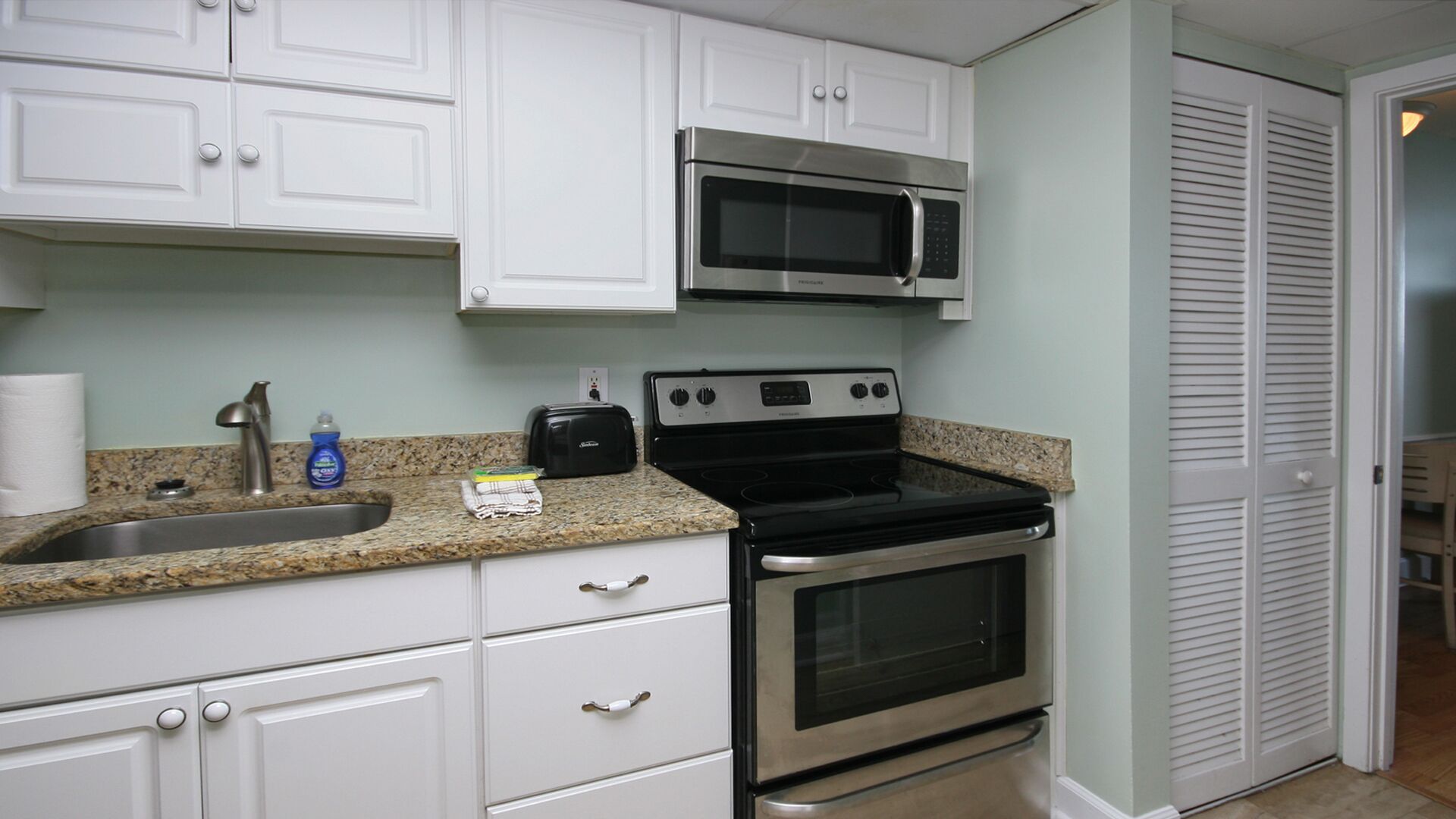 A kitchen with white cabinets, a stainless steel stove, a microwave, and a granite countertop.