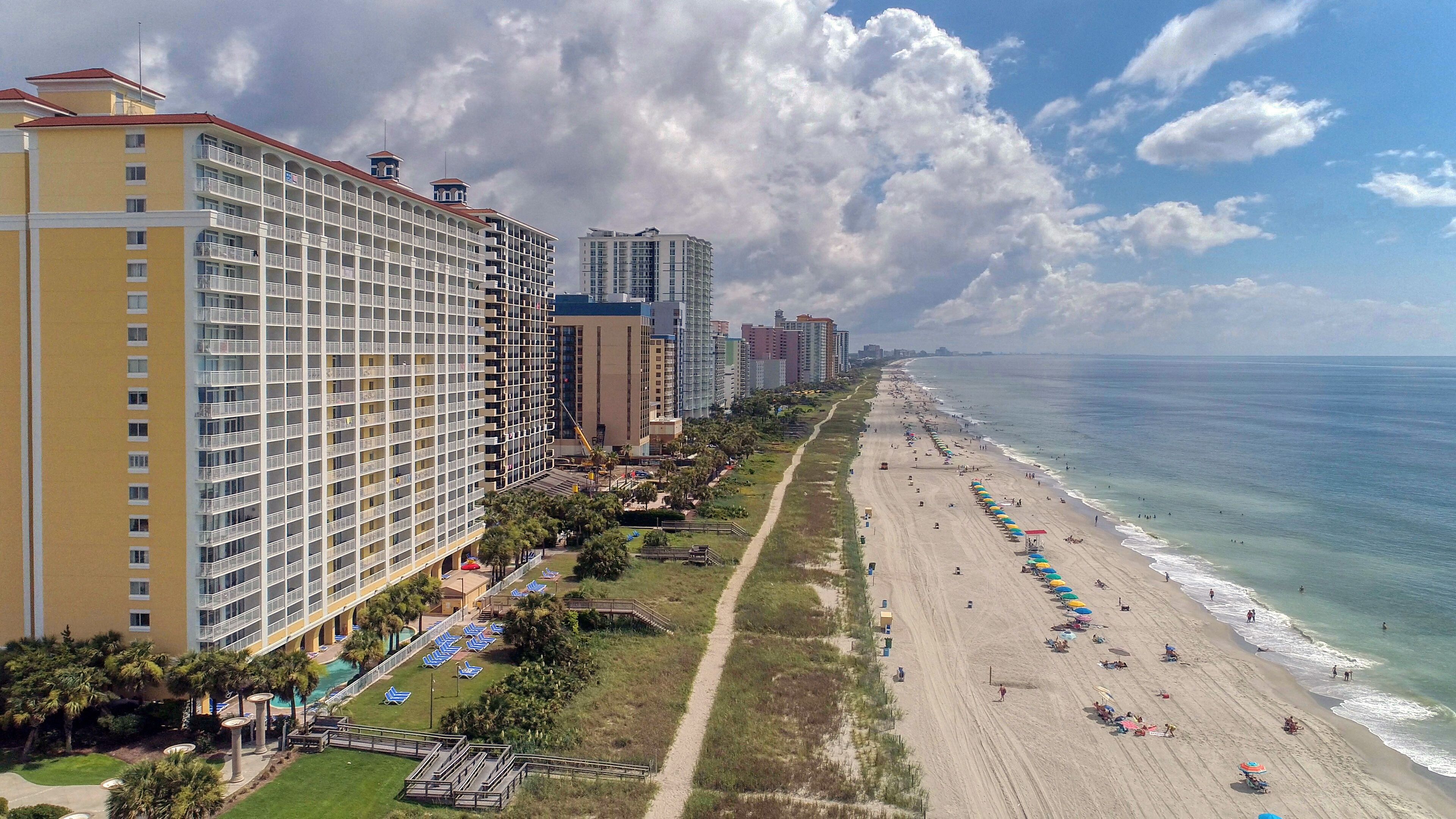 Un hotel costero con varios pisos, ubicación frente a la playa y zona de piscina.
