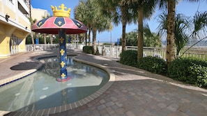 Un espace piscine agrémenté d’une fontaine décorative, de palmiers et offrant une vue sur la mer.