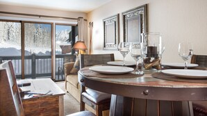 Un comedor con una mesa de madera dispuesta para cuatro personas, ventanas amplias con vista a una montaña nevada y una lámpara sobre la mesa.