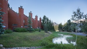 Un edificio con fachada de ladrillo rojo, un área verde con un pequeño estanque y varios árboles.