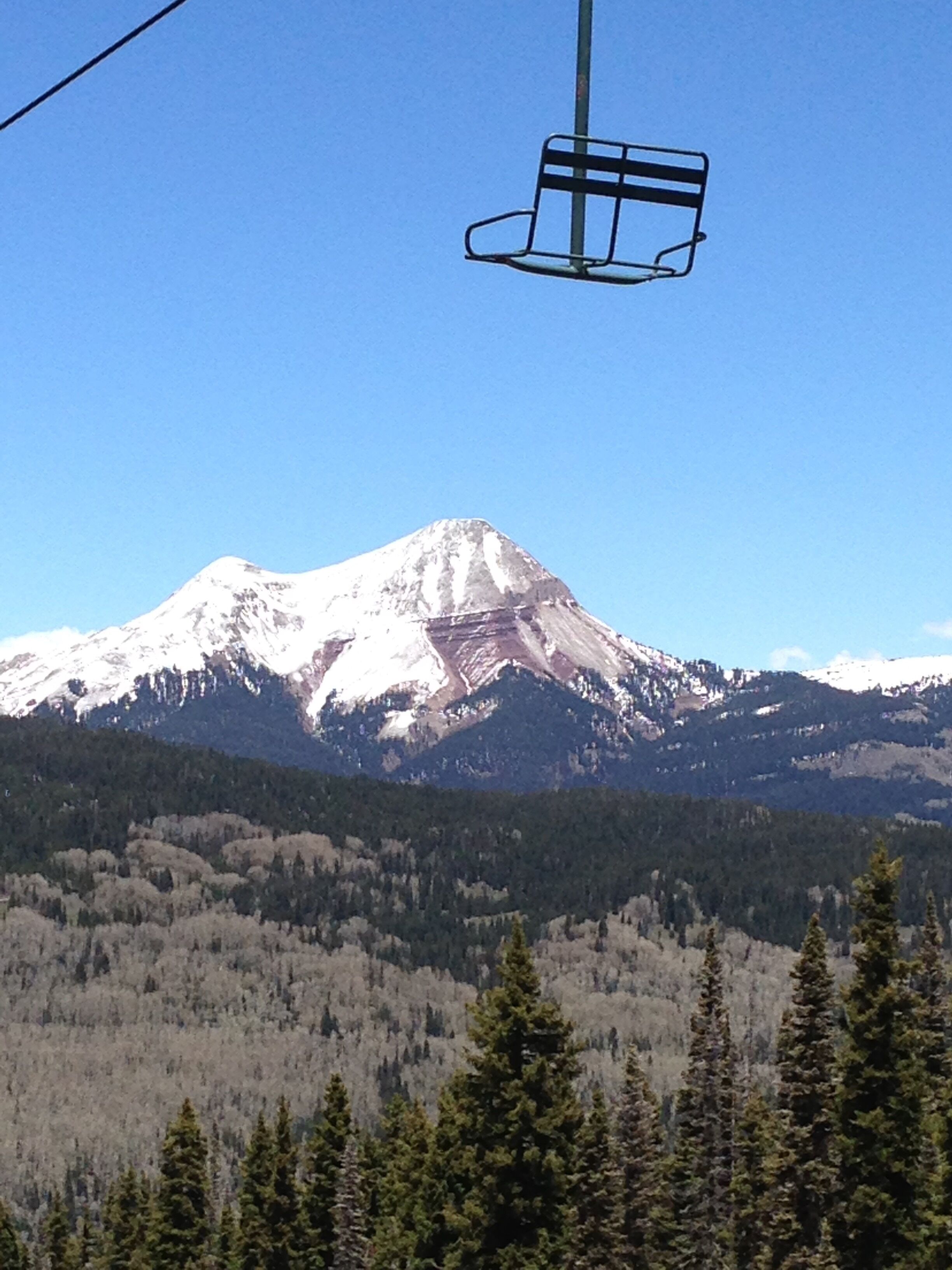 A mountain with a ski lift in the foreground and a forested valley below.